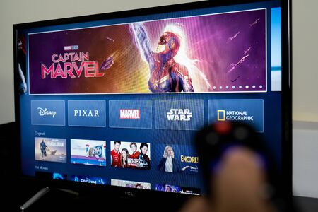 Detroit, USA - Nov 13, 2019: Man holds a remote control with the new online video streaming subscription Disney plus screen on TV.のeditorial素材