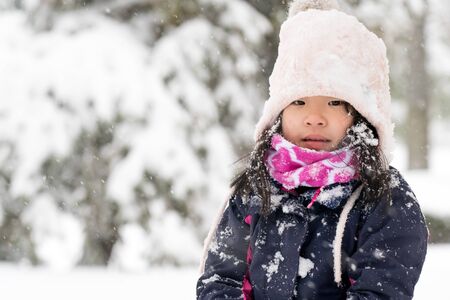 Winter portrait of little asian child girl wearing knitted hat in snow