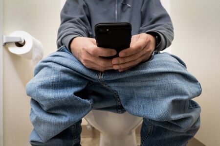 Close up of a man using smart phone in toilet or restroomの写真素材