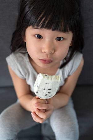 Cute asian toddler girl eating ice cream on couchの写真素材
