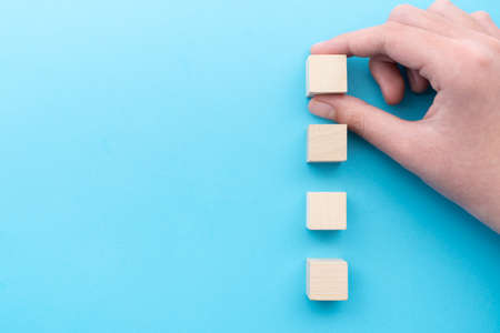 Hand holding a row of four blank wooden cubes in vertical on a blue background, ready for your text.