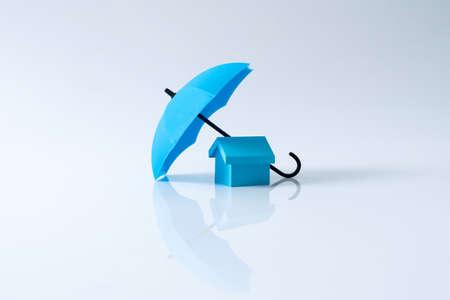 Renters home insurance or mortgage protection concept with a 3D house model under a blue umbrellaの写真素材