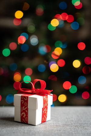 White gift box with red ribbon in front of christmas tree backgroundの写真素材