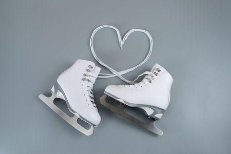 Pair of white figure ice skates shoes on blank gray background, and laces form a heart shapeの写真素材