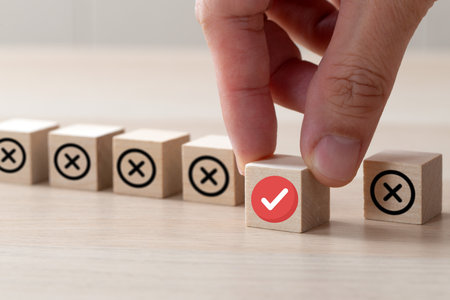Hand picks out wooden cube with checkmark instead of crosses for compliance conceptの写真素材