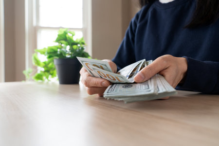 Close-up of female hands counting stack of hundred dollar bills on tableの写真素材
