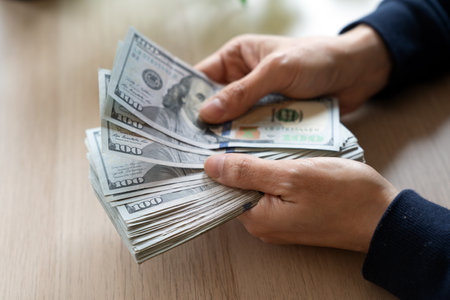 Close-up of female hands counting stack of hundred dollar bills on table