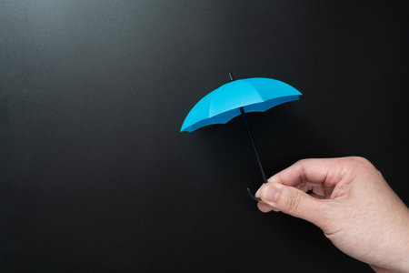 Hand holding mini opened blue umbrella isolated on blank black background