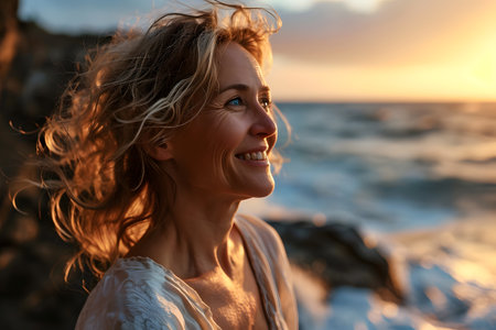 happy middle aged woman smiling with serenity with the beach background with her hair blowing in the breezeの素材