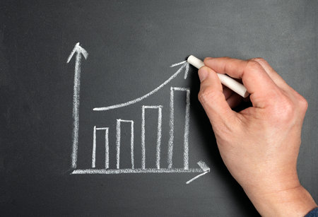 Man hand drawing growing graph with white chalk on blackboard for business growth development planの写真素材