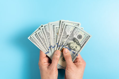Hand holding US hundred dollar money on blue background for concept of investment, financial and successful in business.の写真素材
