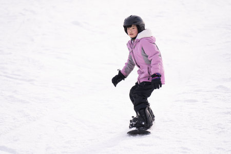 Action motion photo of an Asian female child snowboarder on mountain ski slope doing free snowboarding style.の写真素材