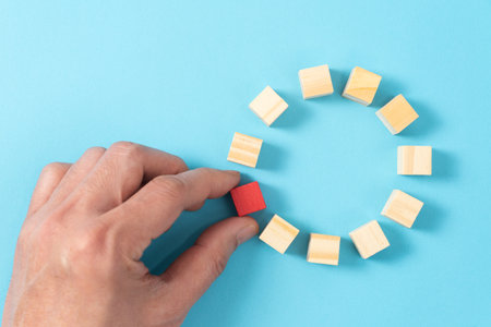 Hand move a single unique red wood block among other wooden cube blocks in round circle, business concept of unique, different, diversity, outstanding, standout or talentの写真素材