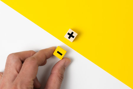 Hand choose a wood block with plus and minus sign on yellow and white background, the concept of opposites, pros and cons, top view compositionの写真素材