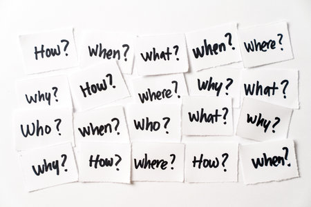 Collection of small paper pieces, each bearing a fundamental question written in black marker How, When, What, Where, Why and Who, symbolizing inquiry, curiosity, and the pursuit of knowledge.の写真素材