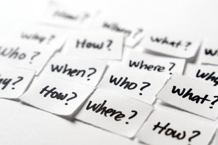 Collection of small paper pieces, each bearing a fundamental question written in black marker How, When, What, Where, Why and Who, symbolizing inquiry, curiosity, and the pursuit of knowledge.の写真素材