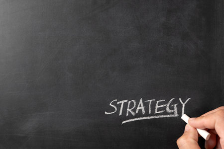 Close-up of a hand writing Strategy on blackboard with white chalk indicating business or marketing planning, with copy space for textの写真素材