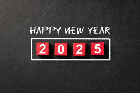 Red wooden cubes 2025 and written happy new year with white chalk on blackboard indicating the...