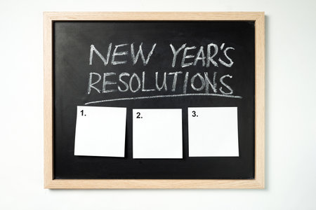Chalkboard with the words New Years Resolutions written in white chalk at the top, below three blank...