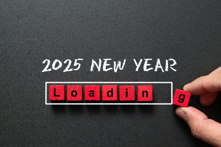 Happy new year 2025 with the word loading spelled out in red wood blocks, symbolizing the upcoming year. A hand is placing the final block as the new year counting downの写真素材