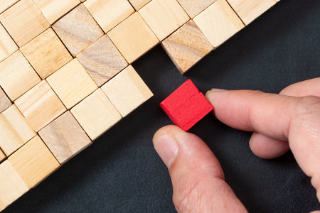Hand choosing a red wooden block from a set isolated on black background. Talent, outstanding and employment conceptの写真素材