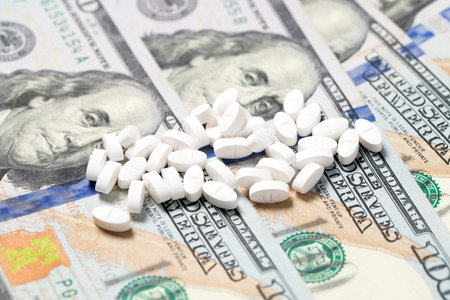 Pile of white medicine pills on US hundred dollars bill for medical expense or prescription drugs cost conceptの写真素材