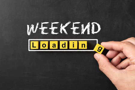 Black chalkboard with a concept of weekend loading bar from yellow wooden blocks with the hand putting in the last blockの写真素材
