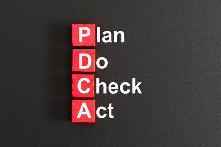 Red wooden cubes with word PDCA, plan, do, check and act in cycle on dark background for continuous improvement on business concept.の写真素材