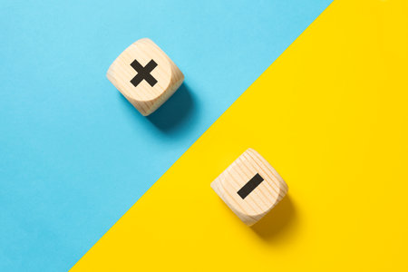 Concept of contrast, opposites, pros and cons with wood block plus and minus sign on blue and yellow background, lay flat compositionの写真素材