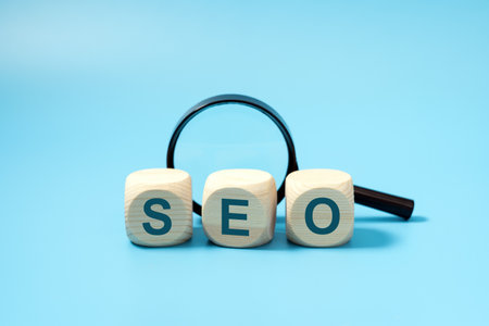 SEO, Search Engine Optimization text wooden cube blocks with a magnifying glass on blue background, idea of strategy, advertising, marketing, keyword and content conceptの写真素材