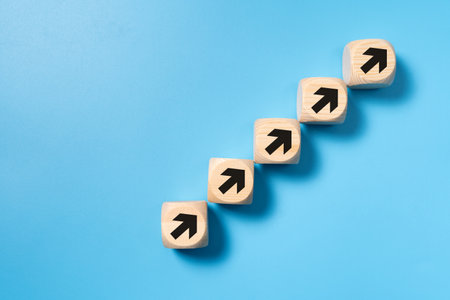 A stack of wooden blocks with arrows pointing upwards for business, sales, revenue or investment growth concept isolated on blue backgroundの写真素材