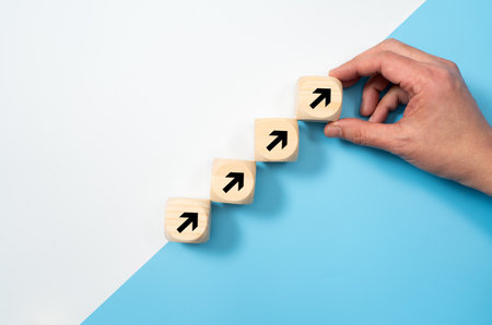 Hand placing wooden blocks with arrows pointing upwards for business, sales, revenue or investment growth concept isolated on white and blue backgroundの写真素材