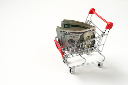 Red miniature shopping cart filled with US dollar banknotes isolated on white background, concept of inflation or budgetingの写真素材