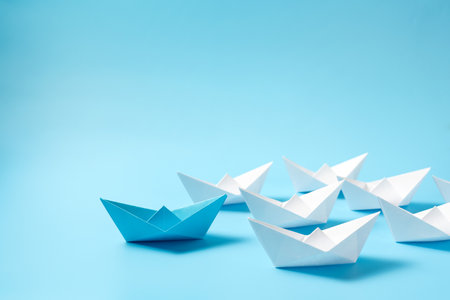Leadership concept with blue paper ship leading among white boats isolated on blue backgroundの写真素材
