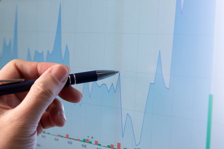 Man hand with pen pointing at financial stock graph on monitor screen, financial and trading concept.の写真素材
