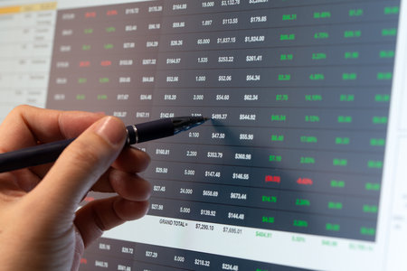 Man hand with pen pointing at financial stock table on monitor screen, financial and trading concept.の写真素材