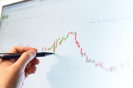 Hand of trader with pen checking stock market data, candlesticks chart on monitor screenの写真素材