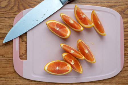 Orange wedges or slices on pink plastic cutting board with a knifeの写真素材