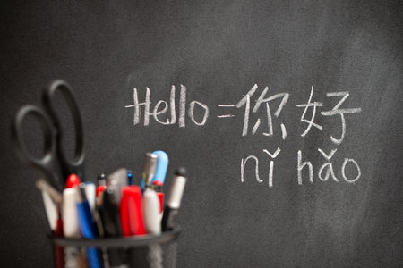 Beginner Chinese language learner writing Hello word Nihao in Chinese characters and pinyin on a chalkboard, concept of learning mandarinの写真素材