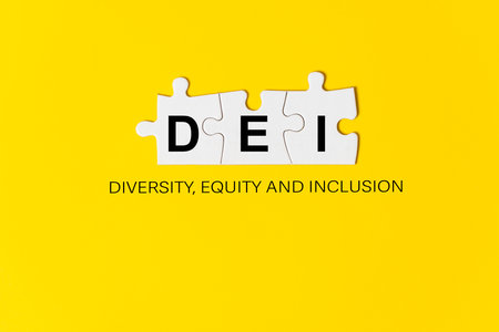 DEI letters written on three pieces of jigsaw puzzle yellow background, which means diversity, equity and inclusion.の写真素材