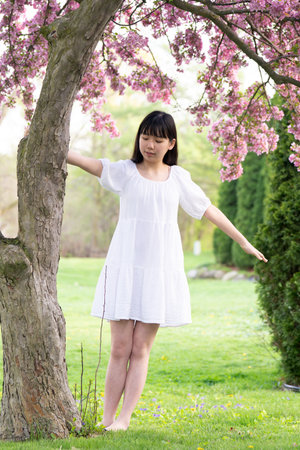 A portrait of a girl teen in a white dress smiling under a tree covered in vibrant pink flowers, set in springtime.の写真素材