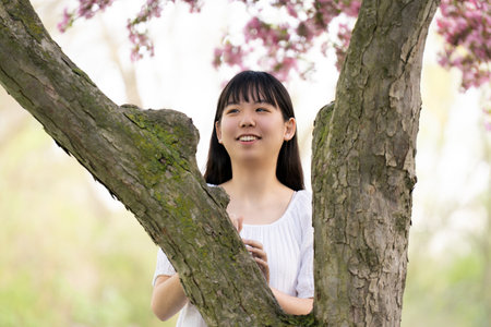 A portrait of a girl teen in a white dress smiling under a tree covered in vibrant pink flowers, set in springtime.の写真素材