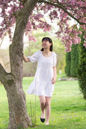 A portrait of a girl teen in a white dress smiling under a tree covered in vibrant pink flowers, set in springtime.の写真素材