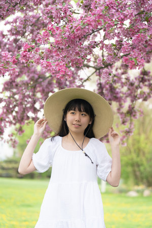 A portrait of a girl teen in a white dress smiling under a tree covered in vibrant pink flowers, set in springtime.の写真素材