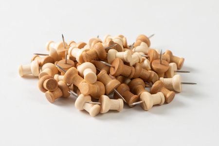 A large pile of wooden pushpins, or thumbtacks on a clean white background. The pushpins have a natural wood grain and various shades of brown.の写真素材