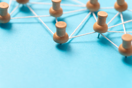 Wooden pushpins or thumbtacks connected by white string on a blue background, illustrating a social media network, people connection, or concept map.の写真素材