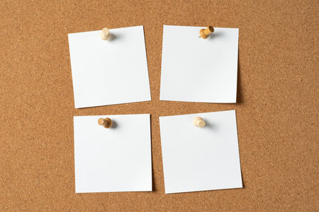 Four blank white notes pinned to a cork bulletin board with wooden push pins, creating space for...