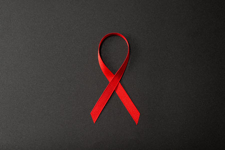Closeup red ribbon symbolize HIV, world AIDS day awareness ribbon on black background, healthcare and medicine concept.の写真素材