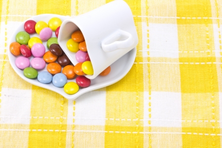 This is a picture of colorful chocolate and coffee cup placed on the table cloth.の写真素材