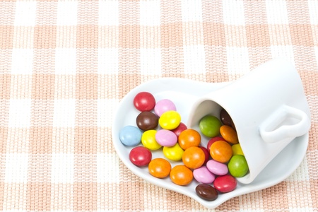 This is a picture of colorful chocolate and coffee cup placed on the table cloth.の写真素材